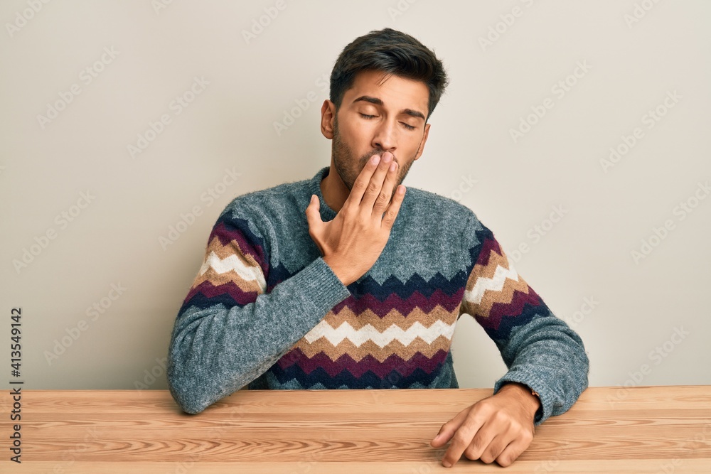 Young handsome man wearing casual sweater sitting on the table bored yawning tired covering mouth with hand. restless and sleepiness. Young handsome man wearing casual sweater sitting on the table bored yawning tired covering mouth with hand. restless and sleepiness.
