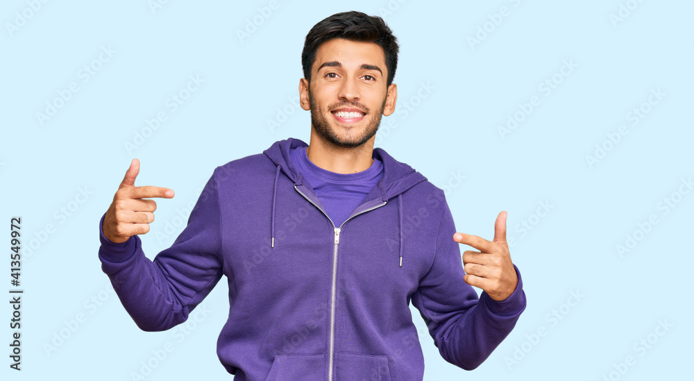 Fototapeta premium Young handsome man wearing casual sweatshirt looking confident with smile on face, pointing oneself with fingers proud and happy.