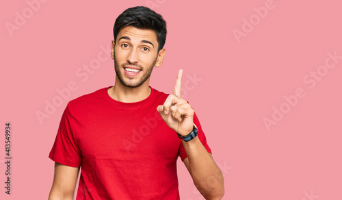 Young handsome man wearing casual red tshirt pointing finger up with successful idea. exited and happy. number one.