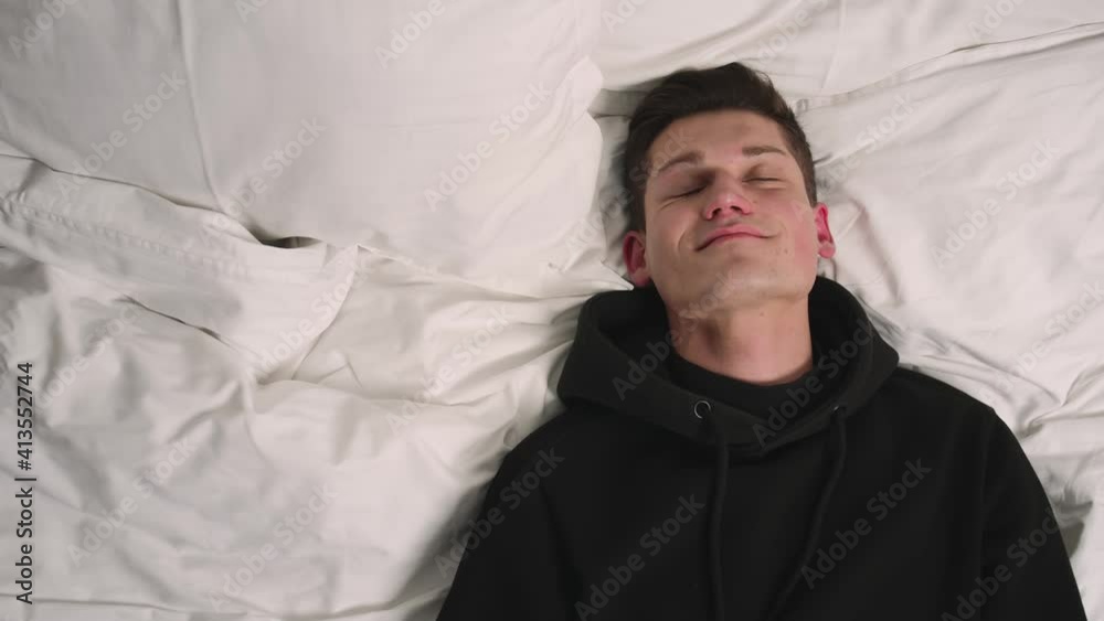 Smiling handsome man goes to sleep in comfortable cozy fresh bed enjoying healthy good sleep nap. Man falling on the bed. Smiling handsome man goes to sleep in comfortable cozy fresh bed enjoying healthy good sleep nap. Man falling on the bed.