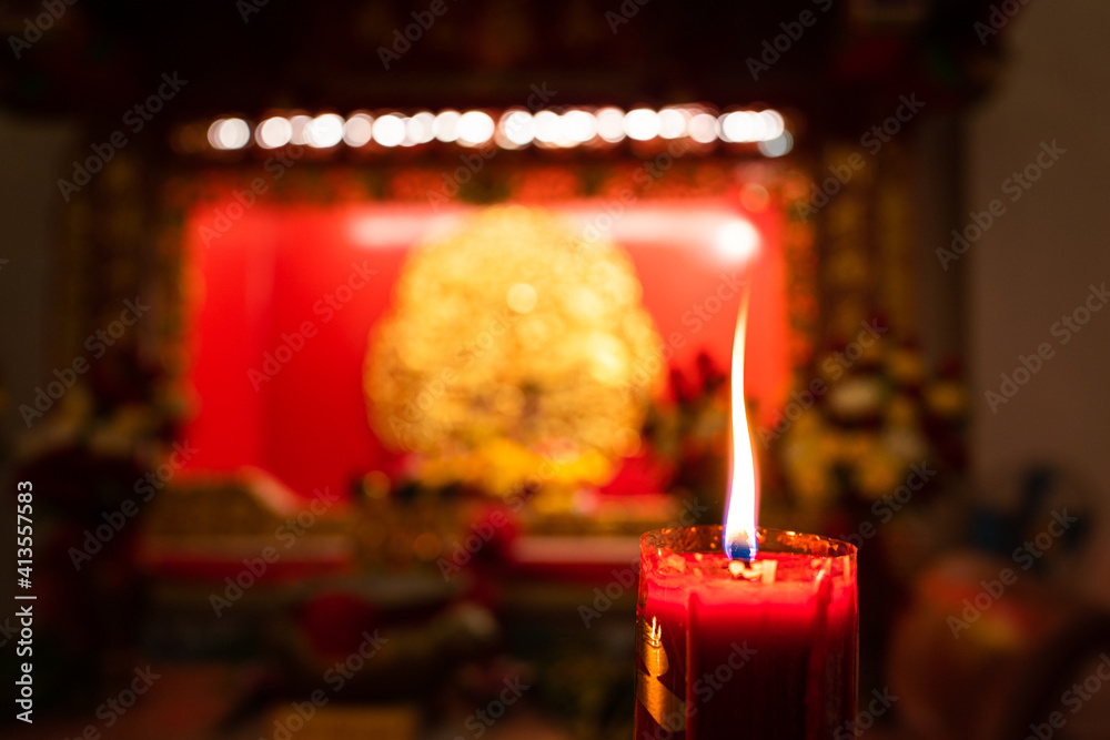 Close-up at candlelight during in burning with blurred background of the Chinese shrine. Selective focus the at the candle's core. Close-up at candlelight during in burning with blurred background of the Chinese shrine. Selective focus the at the candle's core.
