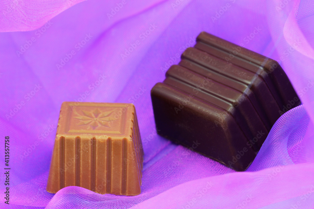 Milk and dark chocolates on purple colour textile with copy space