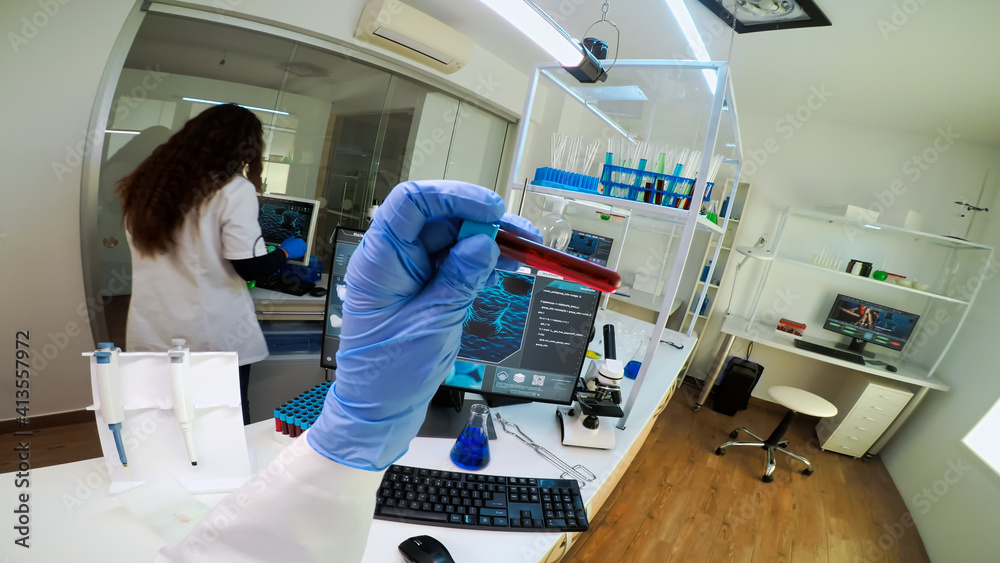 Naklejka premium FPV of scientist holding blood sample from test tube analysing and typing on pc vaccine evolution. Team of doctors, viorolog researcher in professional lab working to discover medical treatment.