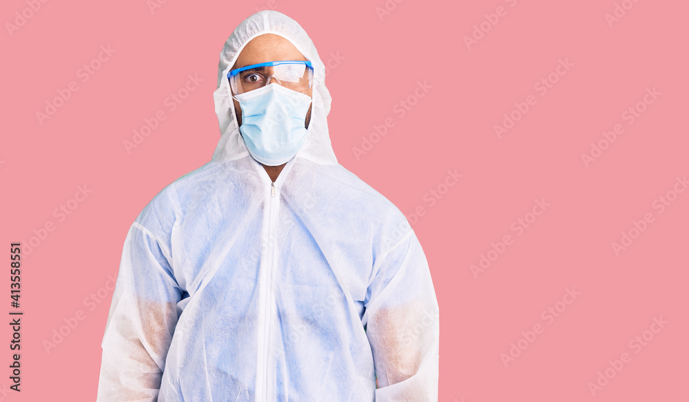 Young hispanic man wearing doctor protection coronavirus uniform and medical mask afraid and shocked with surprise expression, fear and excited face. Young hispanic man wearing doctor protection coronavirus uniform and medical mask afraid and shocked with surprise expression, fear and excited face.