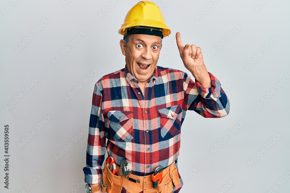 Senior hispanic man wearing handyman uniform pointing finger up with successful idea. exited and happy. number one.