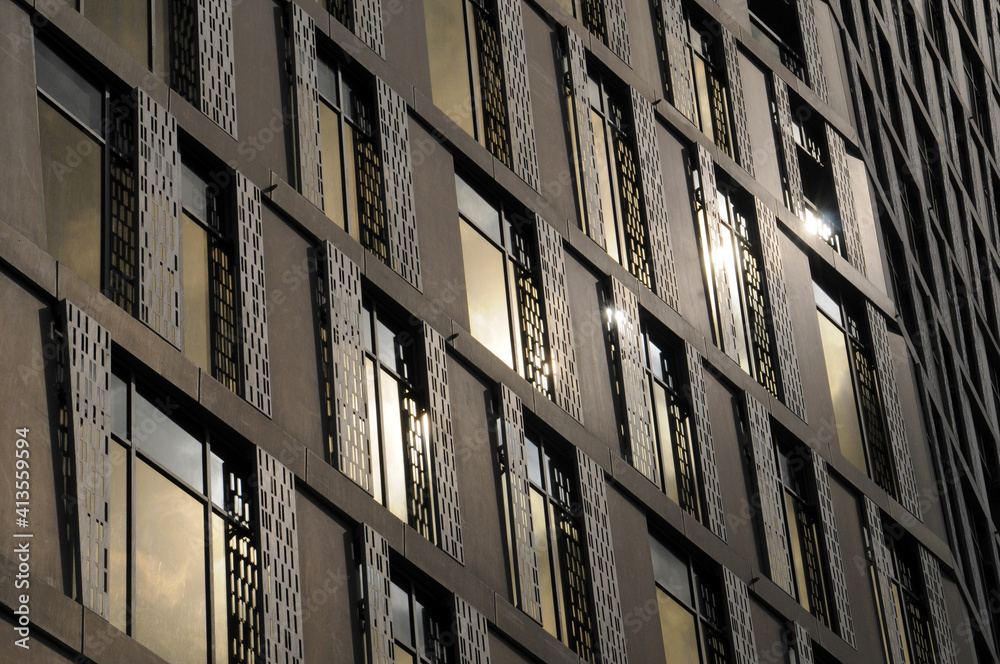 Vue sur une façade métallique brillante bronze et cuivre, vitrages rectangulaires en verre, structures en croix et reflets dorés et blancs du soleil.