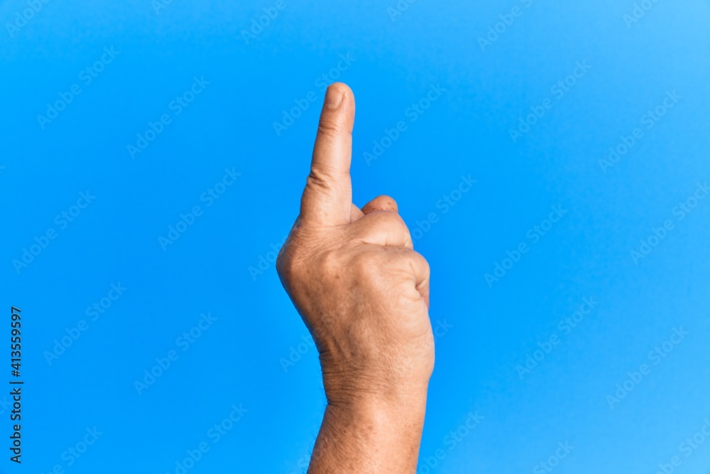 Hand of senior hispanic man over blue isolated background showing provocative and rude gesture doing fuck you symbol with middle finger