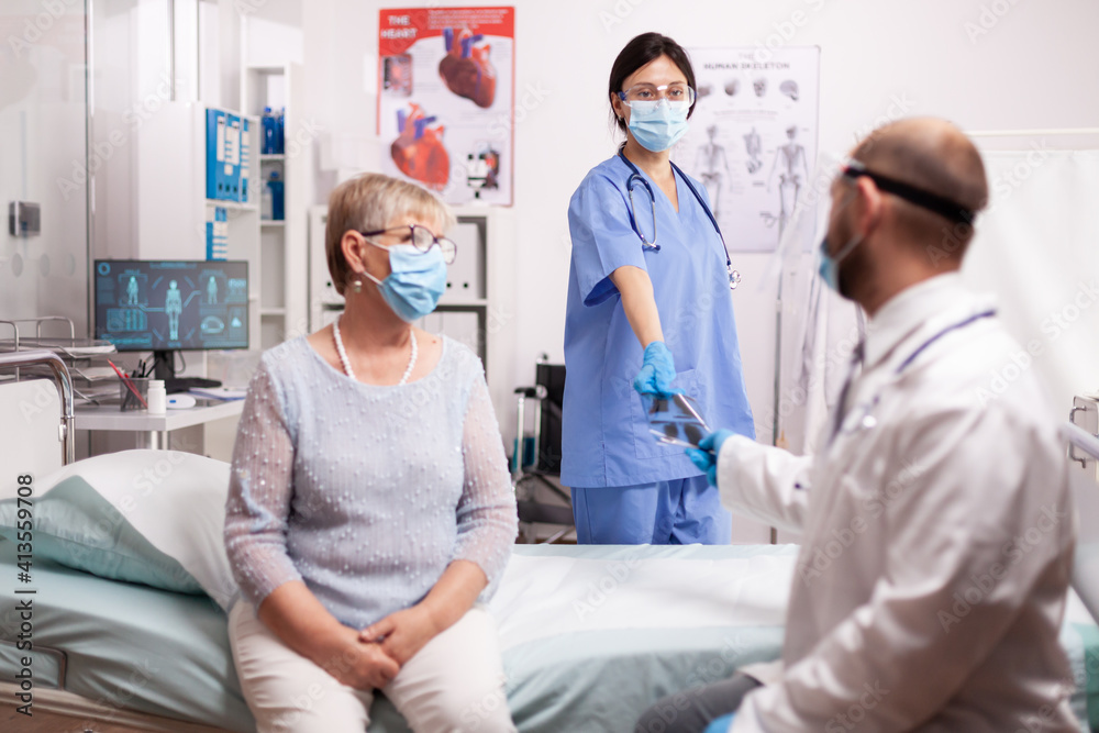 Nurse giving doctor senior patient x-ray wearing face mask as safety precaution in the course of covid19 outbreak. Medical practitioner checking patient lungs looking at radiography during coronavirus