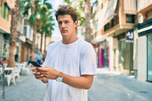 Young caucasian man with serious expression using smartphone and smoking cigarette at the city.