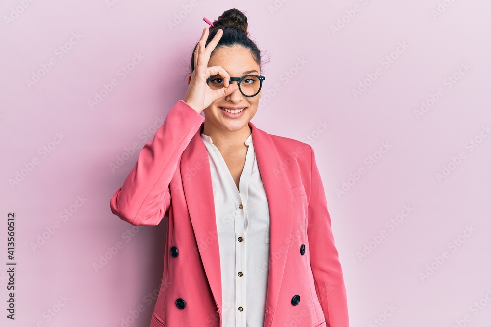 Beautiful middle eastern woman wearing business jacket and glasses doing ok gesture with hand smiling, eye looking through fingers with happy face.