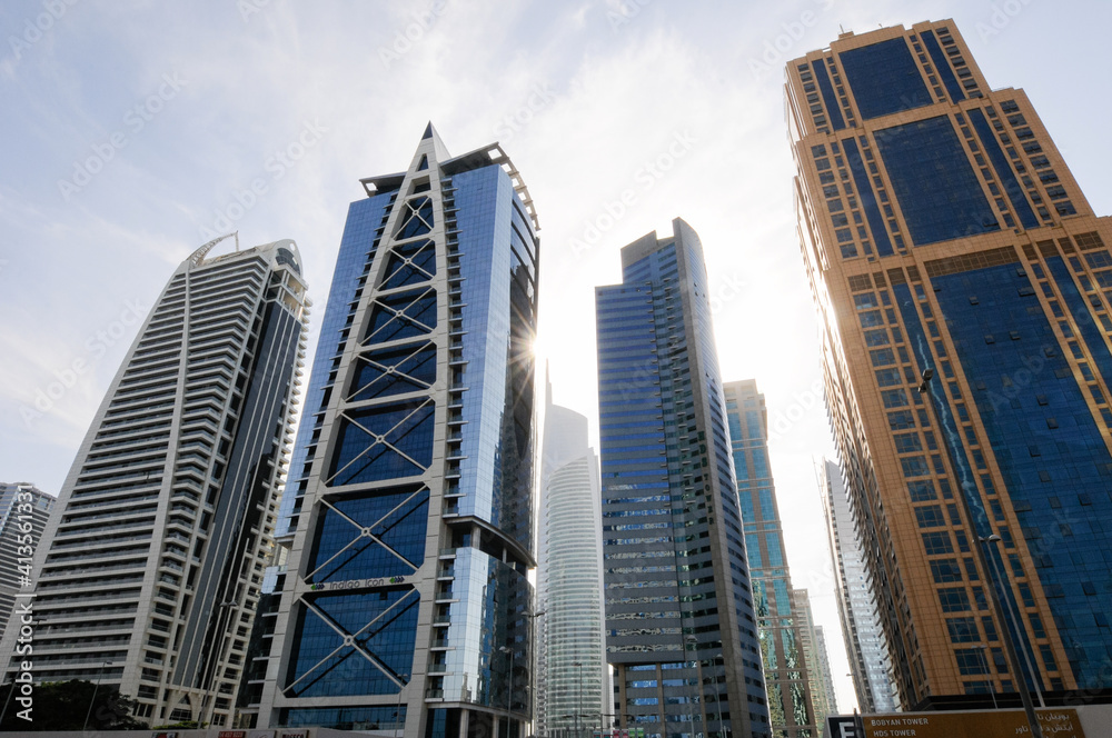 7 gratte-ciel ou buildings de Dubaï se dressant vers le ciel bleu. Nouveaux bâtiments vitrés à l'architecture moderne, présentant diverses lignes et courbes géométiques au soleil couchant et brillant.