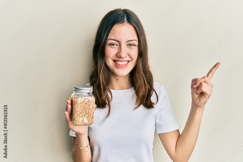 Young brunette woman holding jar with rice smiling happy pointing with hand and finger to the side Young brunette woman holding jar with rice smiling happy pointing with hand and finger to the side
