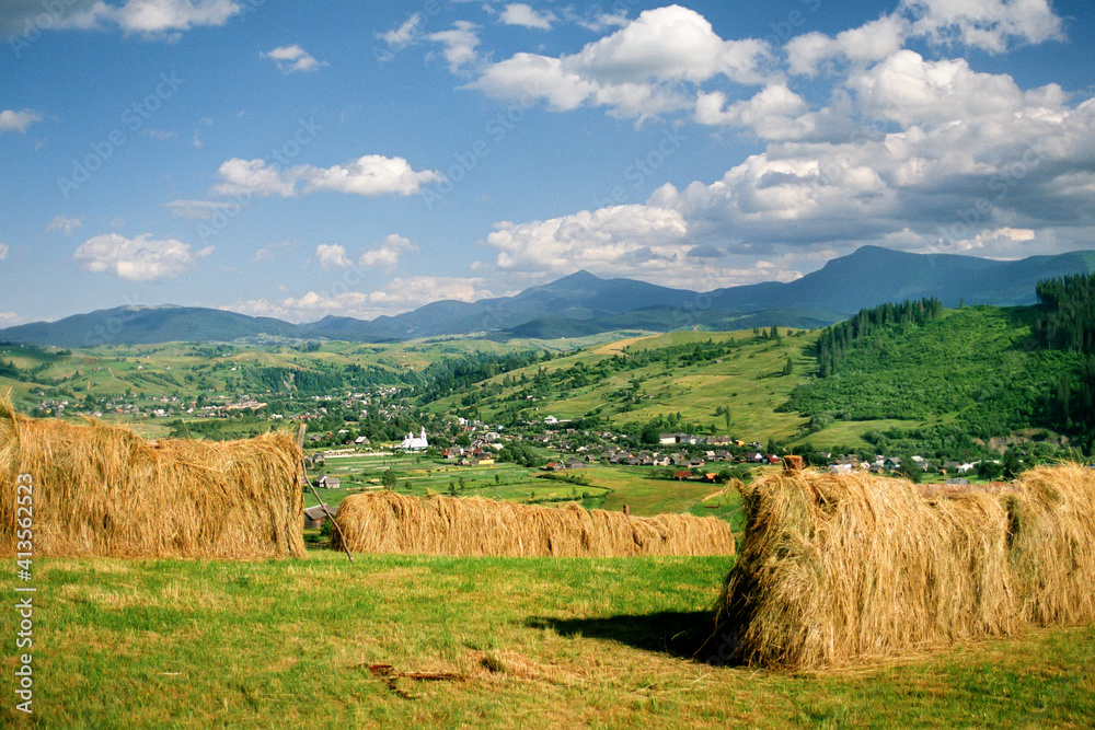 Drying hay on the background of a mountain village in the Carpathian mountains with blue sky and white clouds