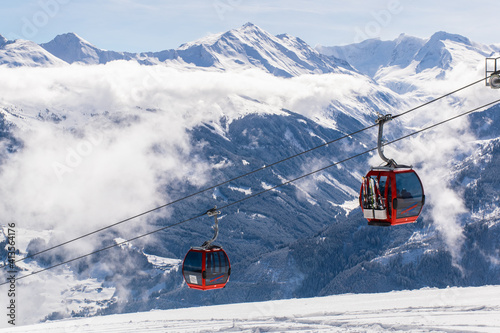 Cable car in the Austrian Alps in winter near Kitzbuhel. Behind the snow-covered fir trees  illuminated by the sun  the majestic mountain peaks rise against the blue sky.