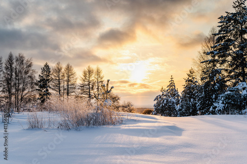 Frosty winter landscape at sunset in forest, sunbeam breaks clouds