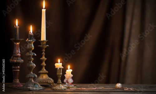 antique candlestick with burning candle on old wooden table on background brown velvet curtain photo