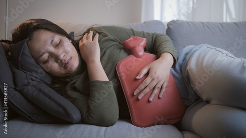 Sick woman with heavy menstrual cramps is applying hot water bag on her stomach