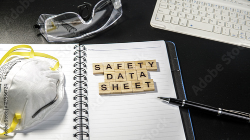 Safety Data Sheet wording on table with keyboard, safety spectacles, notebook and N95 Dust mask