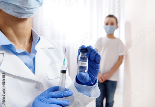 Vial with vaccine and syringe in the hands of pediatrician on the blurred background of a little boy
