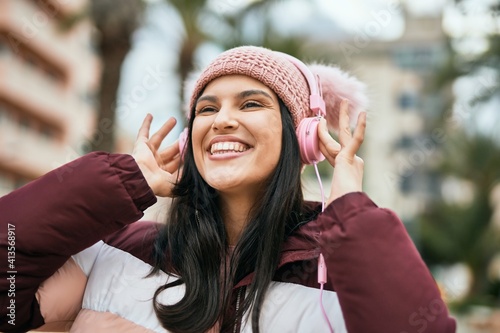 Young hispanic girl smiling happy using headphones at the city.