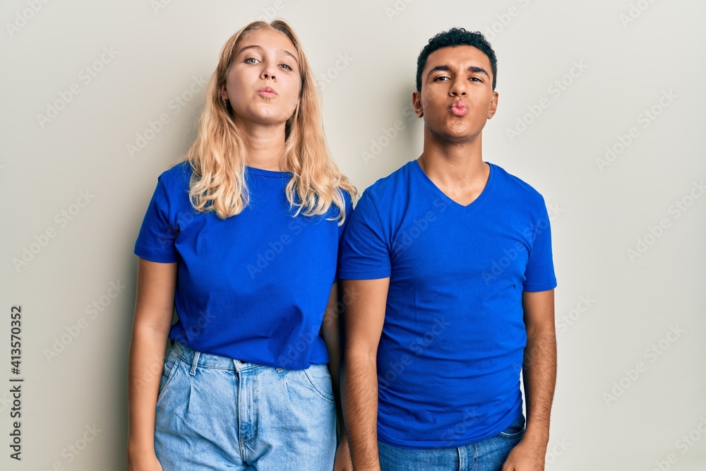 Young interracial couple wearing casual clothes looking at the camera blowing a kiss on air being lovely and sexy. love expression. Young interracial couple wearing casual clothes looking at the camera blowing a kiss on air being lovely and sexy. love expression.