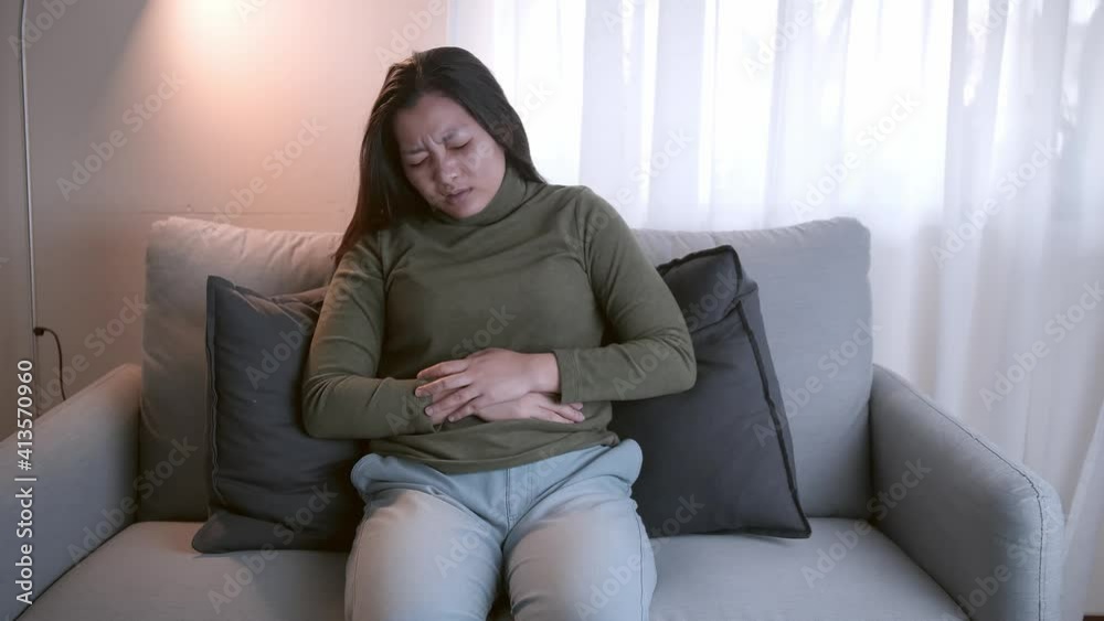 The woman with severe abdominal pain and abdominal pain in her body for unknown reasons lies on the sofa in the living room. The woman with severe abdominal pain and abdominal pain in her body for unknown reasons lies on the sofa in the living room.