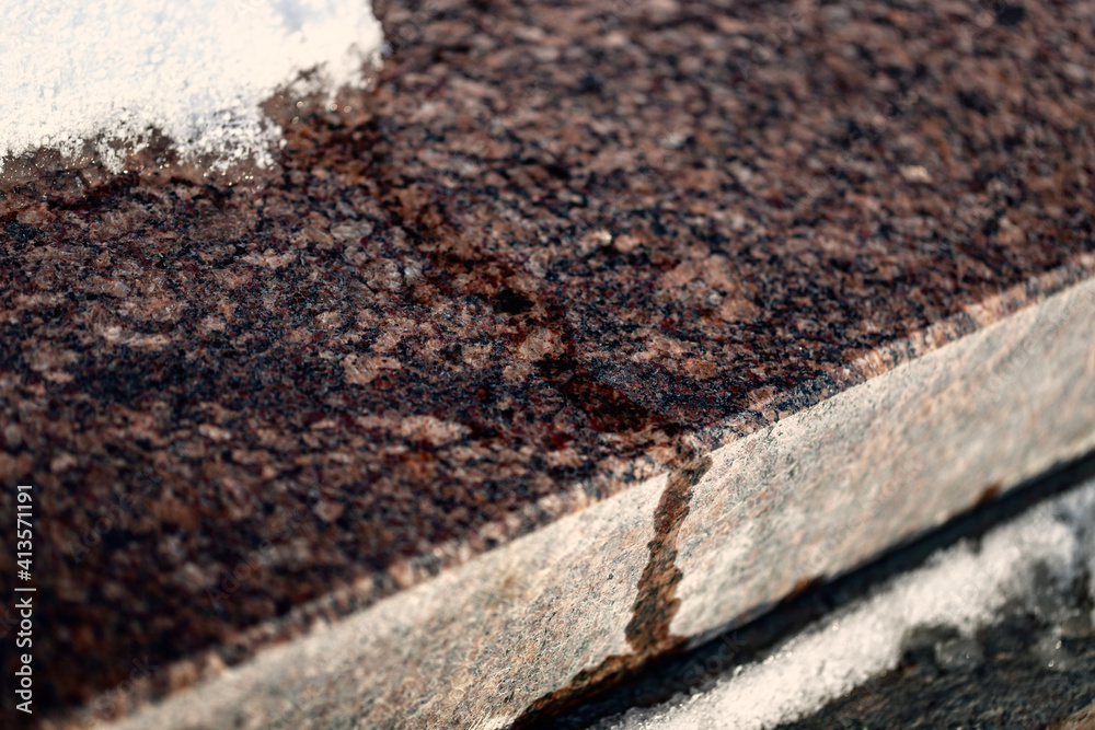 polished granite surface with slowly melting snow / purple brown smooth shiny stone polished granite surface with slowly melting snow / purple brown smooth shiny stone