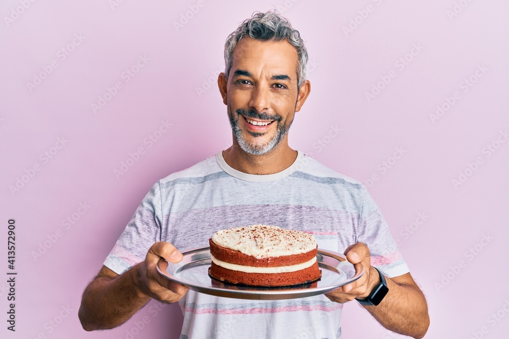 Middle age grey-haired man holding carrot cake smiling with a happy and cool smile on face. showing teeth. Middle age grey-haired man holding carrot cake smiling with a happy and cool smile on face. showing teeth.