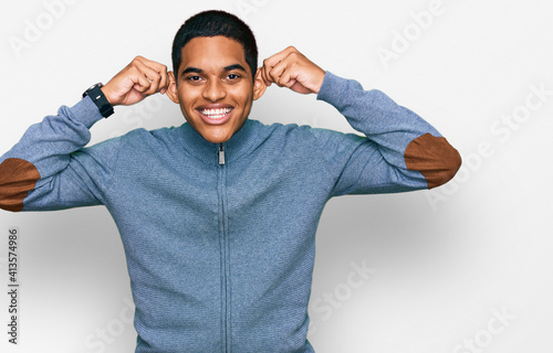 Young handsome hispanic man wearing casual sweatshirt smiling pulling ears with fingers, funny gesture. audition problem