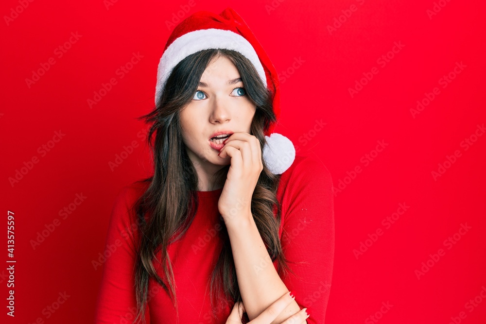 Young beautiful caucasian girl wearing christmas hat looking stressed and nervous with hands on mouth biting nails. anxiety problem. Young beautiful caucasian girl wearing christmas hat looking stressed and nervous with hands on mouth biting nails. anxiety problem.