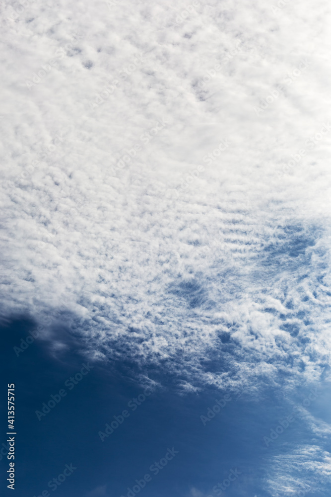 Blue summer sky with white clouds, vertical frame.