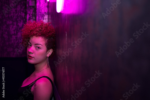 Woman with light colored cardigan posing under neon light