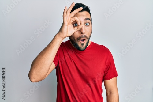 Young hispanic man wearing casual clothes doing ok gesture shocked with surprised face, eye looking through fingers. unbelieving expression.