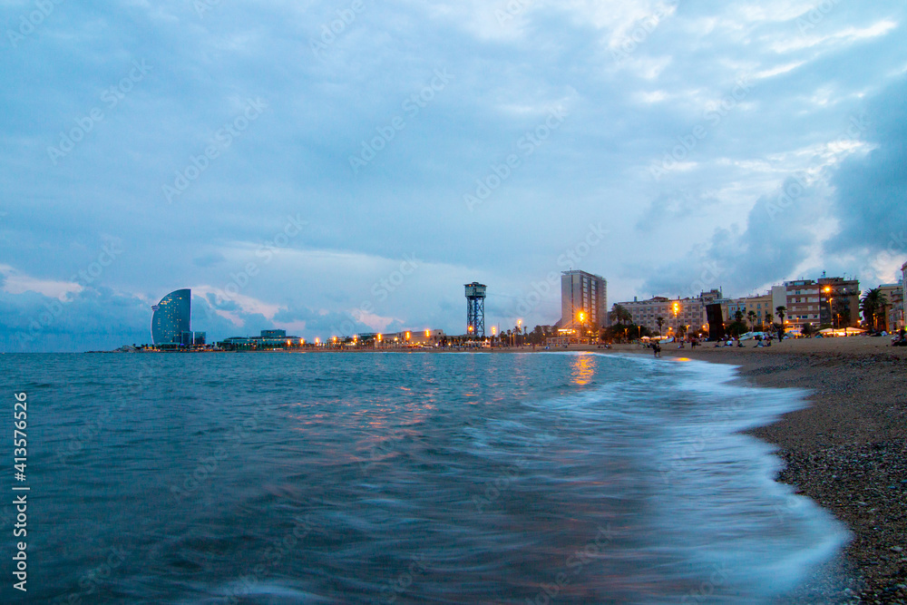 Barcelona Beach in summer night along seaside in Barcelona, Catalonia, Spain. Barceloneta landscape after sunset in blue hour. Mediterranean Sea. Europe tourism and modern city life concept.