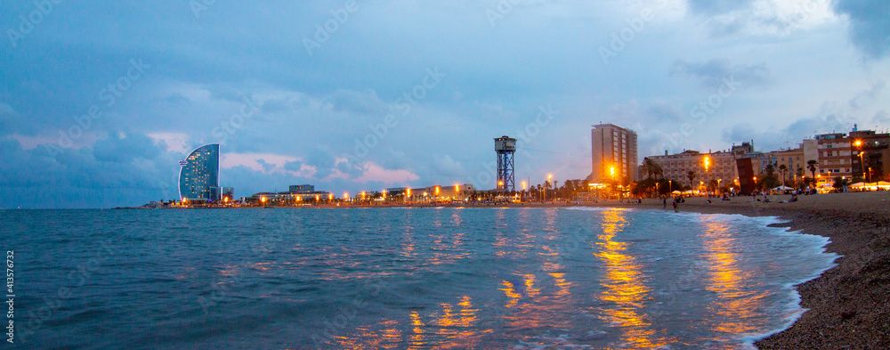 Barcelona Beach panorama in summer night along seaside in Barcelona, Catalonia, Spain. Barceloneta landscape after sunset in blue hour. Mediterranean Sea. Europe tourism and modern city life concept.