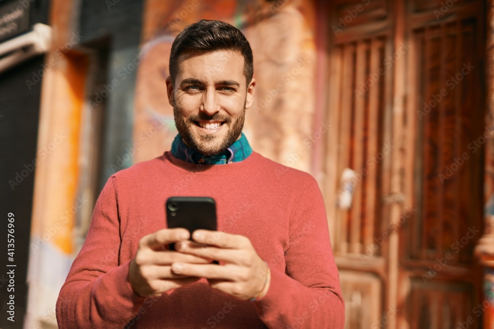 Young hispanic man smiling happy using smartphone at the city.