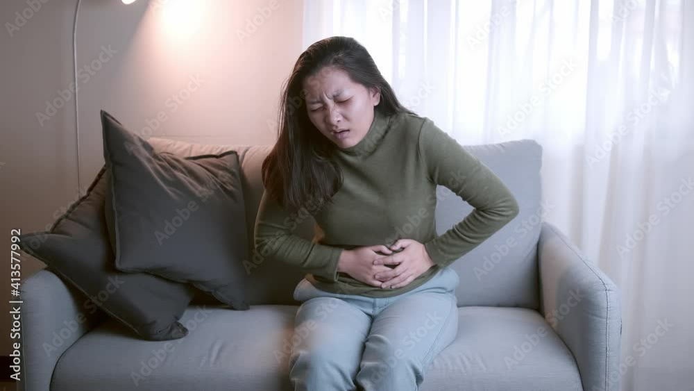 The woman with severe abdominal pain and abdominal pain in her body for unknown reasons lies on the sofa in the living room. The woman with severe abdominal pain and abdominal pain in her body for unknown reasons lies on the sofa in the living room.