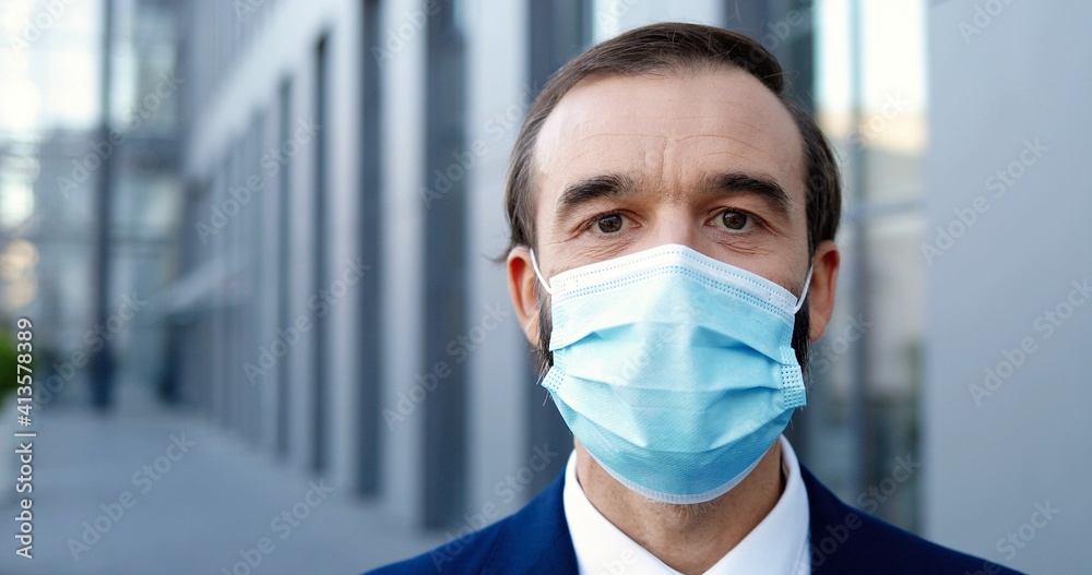 Portrait of Caucasian middle-aged man in medical mask standing outside and looking at camera. Pandemic coronavirus concept. Close up of male businessman in respiratory protection. Pandemic.