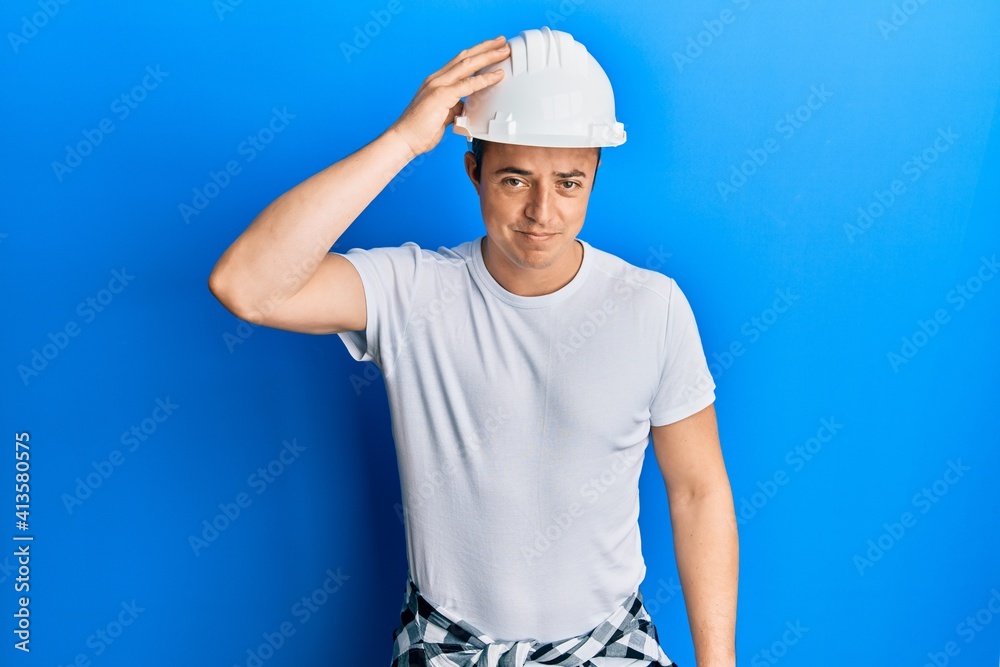 Handsome young man wearing builder uniform and hardhat confuse and wonder about question. uncertain with doubt, thinking with hand on head. pensive concept.