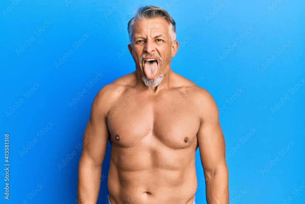 Middle age grey-haired man standing shirtless sticking tongue out happy with funny expression. emotion concept.