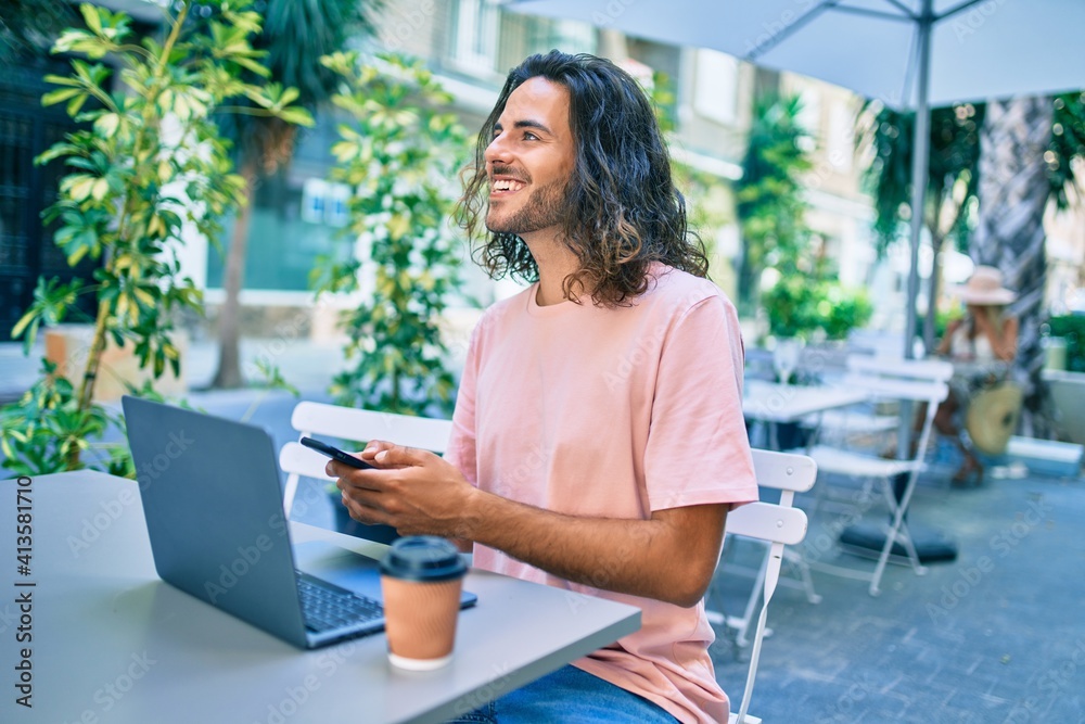 Young hispanic man smiling happy working using laptop and smartphone at terrace of coffee shop. Young hispanic man smiling happy working using laptop and smartphone at terrace of coffee shop.