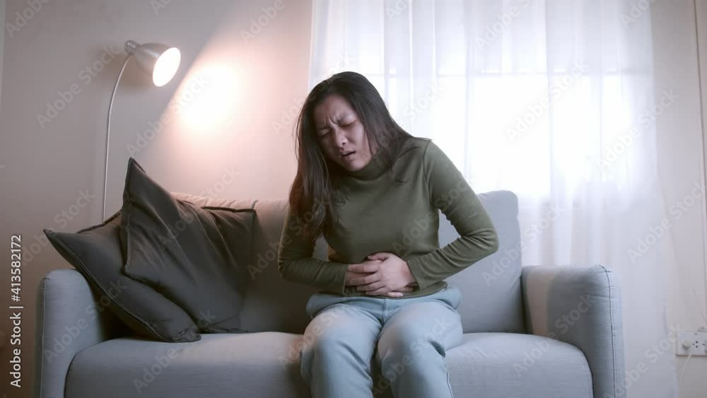 The woman with severe abdominal pain and abdominal pain in her body for unknown reasons lies on the sofa in the living room. The woman with severe abdominal pain and abdominal pain in her body for unknown reasons lies on the sofa in the living room.
