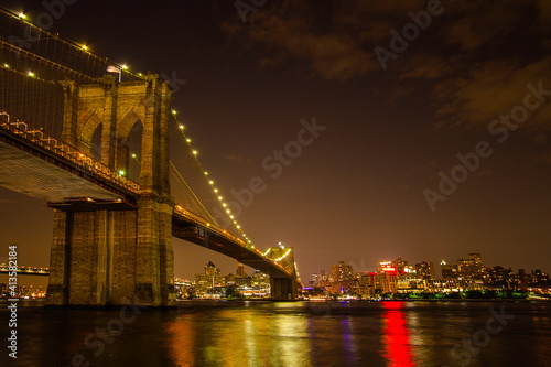 The night view of the Brooklyn Bridge with the city lights reflections on East River 