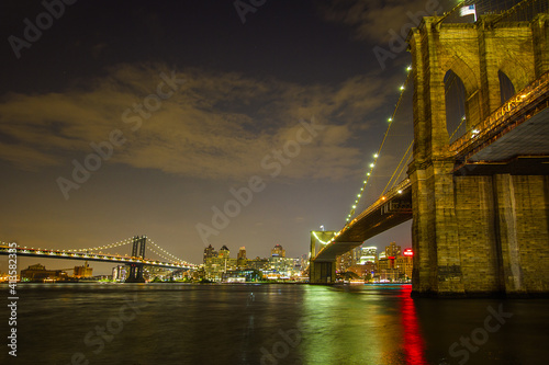 The view of the Brooklyn Bridge from Manhattan at night with the reflection of the city light on East River and Manhattan Bridge in the background 