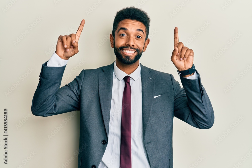 Handsome hispanic man with beard wearing business suit and tie smiling amazed and surprised and pointing up with fingers and raised arms. Handsome hispanic man with beard wearing business suit and tie smiling amazed and surprised and pointing up with fingers and raised arms.