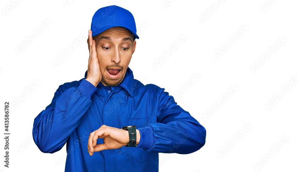 Bald man with beard wearing builder jumpsuit uniform looking at the watch time worried, afraid of getting late Bald man with beard wearing builder jumpsuit uniform looking at the watch time worried, afraid of getting late