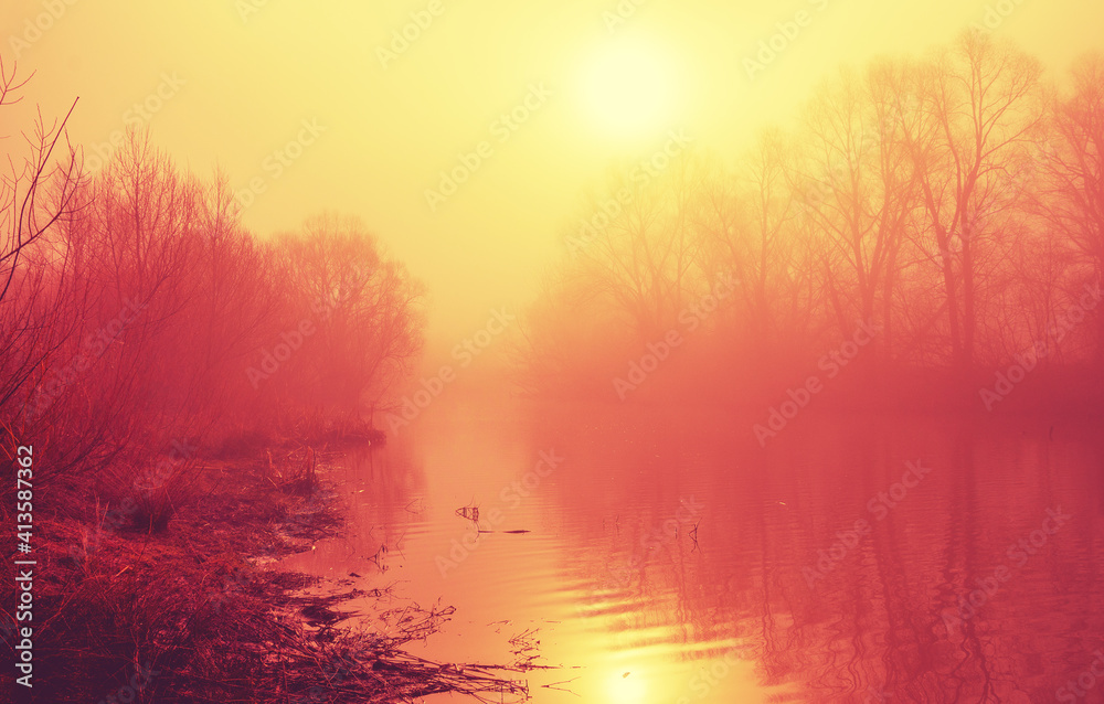 Abstract foggy spring landscape with calm river and bare trees during serene april morning.