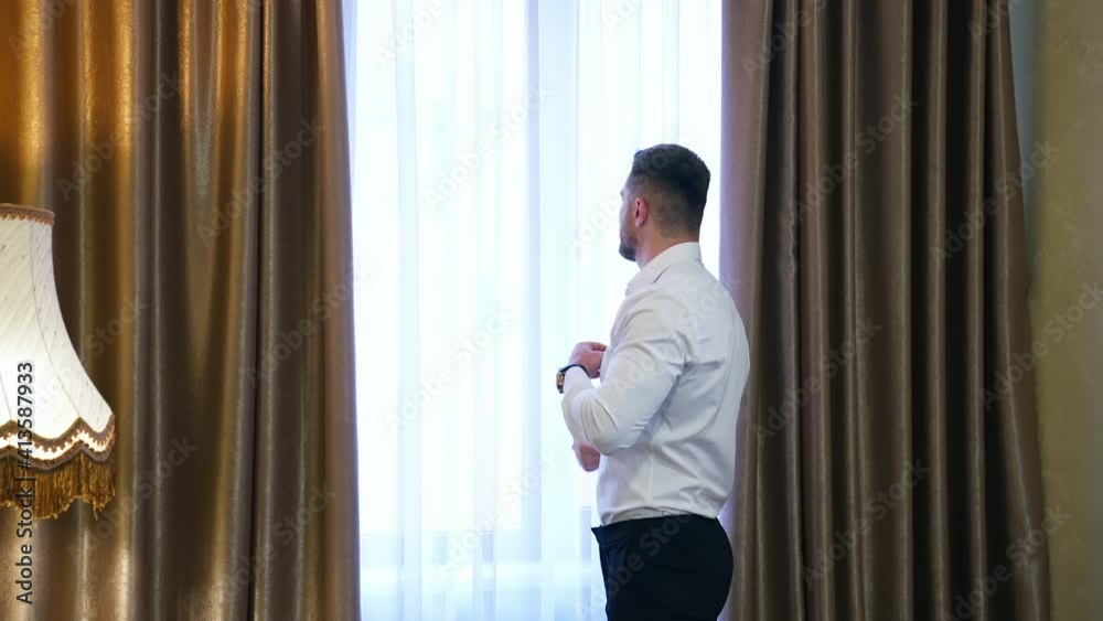 Businessman looking into the window in hotel. Man in white shirt and trousers standing near the window and dreaming. Back view.