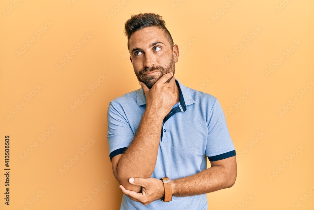 Handsome man with beard wearing casual clothes with hand on chin thinking about question, pensive expression. smiling with thoughtful face. doubt concept.