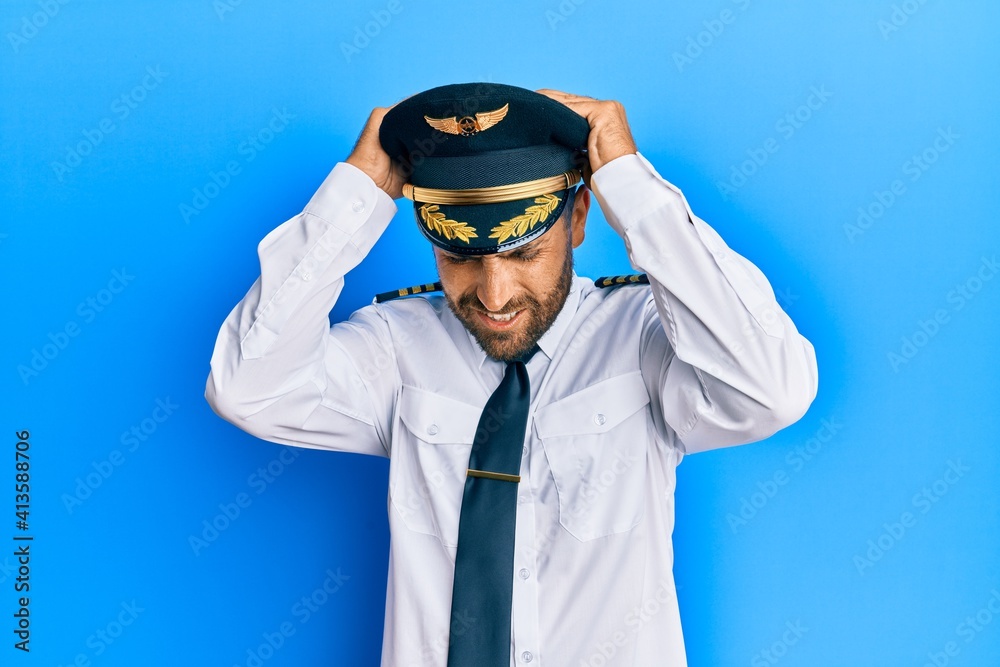 Handsome man with beard wearing airplane pilot uniform suffering from headache desperate and stressed because pain and migraine. hands on head. Handsome man with beard wearing airplane pilot uniform suffering from headache desperate and stressed because pain and migraine. hands on head.